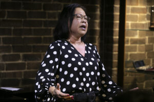 Woman performing on stage. She's wearing polka dots blouse in black and white.